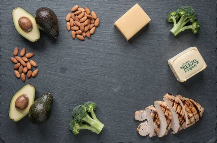 Sélection d'aliments keto disposés en flat lay sur une ardoise sombre : avocat, amandes, fromage, poulet et légumes